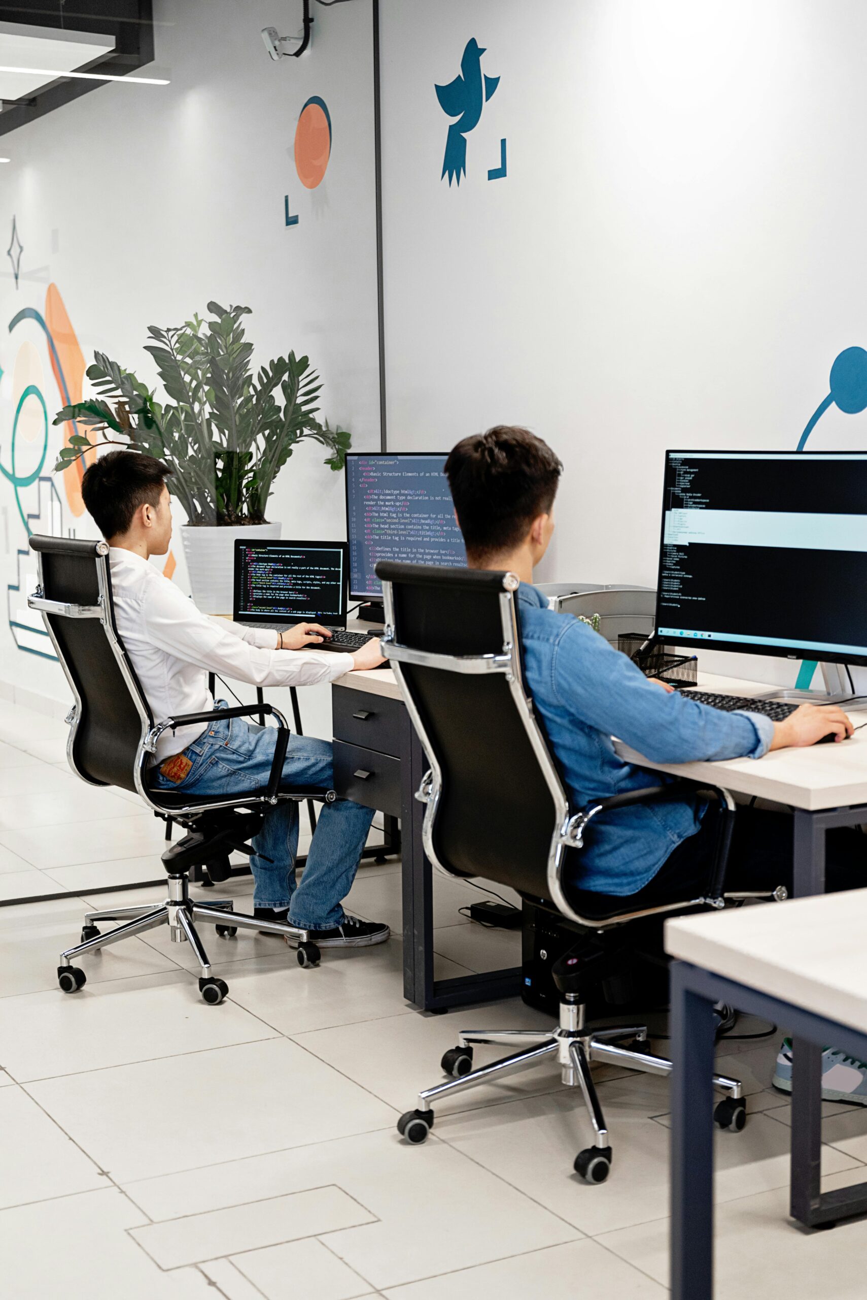 Two programmers collaborating in a bright, modern office, coding on monitors.